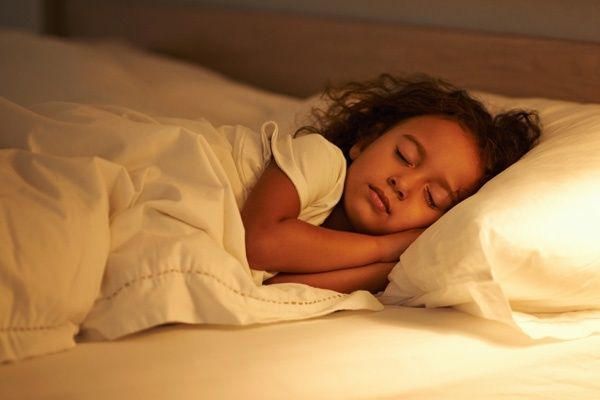 Sleeping child tucked into bed under warm light at bedtime